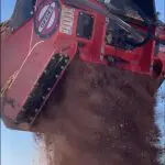 A red truck is dumping dirt on the ground.