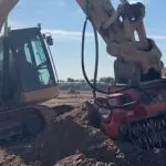 A tractor is digging in the ground with a large pile of dirt.