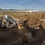 A tractor is digging in the dirt on a field.
