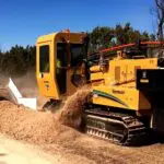 A yellow tractor is cutting the ground with a large machine.