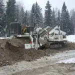 A large machine is digging in the snow.