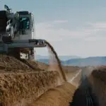 A tractor is dumping dirt on the side of a road.